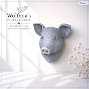 May include: A gray, textured pig head wall mount sculpture featuring prominent ears and a snout. The text "Wolfena's VINTAGE VIBES - CURATED FINDS timeless pieces, lovingly found" is visible in the upper left corner, accompanied by a small fern icon.