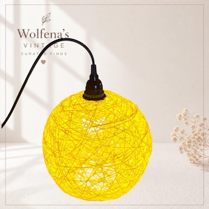 May include: A yellow sphere pendant light with a woven texture. The light hangs from a black cord and fixture. The text "Wolfena's Vintage Curated Finds" is at the top.