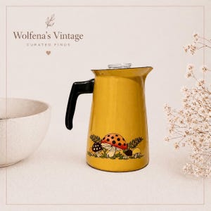 May include: A vintage yellow enamelware coffee pot with a black handle and a clear glass lid. The pot is decorated with a mushroom design. The text "Wolfena's Vintage" is at the top of the image.