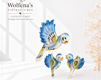 May include: Three ceramic bird figurines featuring blue and yellow hand-painted details with wings spread in flight. The text Wolfena's VINTAGE VIBES CURATED FINDS lovingly chosen just for you is printed in the upper left corner of the image.