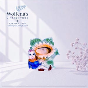 May include: A ceramic planter shaped like a stylized flower with a central opening, featuring a small figure with a blue shirt and red shoes sitting at the base. The flower has green leaves and a yellow-orange center. Text reads Wolfena's VINTAGE VIBES.