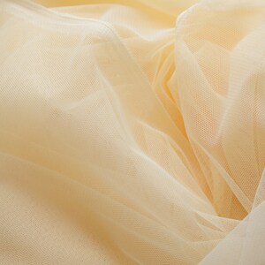 May include: A close-up of a soft, pale yellow tulle fabric. The fabric is delicate and has a fine mesh texture.