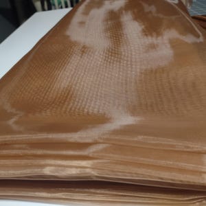 May include: A folded piece of brown sheer fabric with a subtle grid pattern. The fabric is translucent and has a soft, flowing texture.