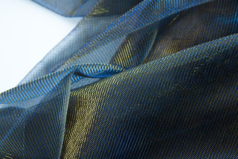 May include: Close-up of a blue and gold metallic fabric with a textured, woven pattern.