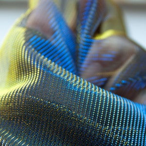 May include: Close-up of a blue and gold fabric with a textured, iridescent finish. The fabric has a subtle pattern of small dots.