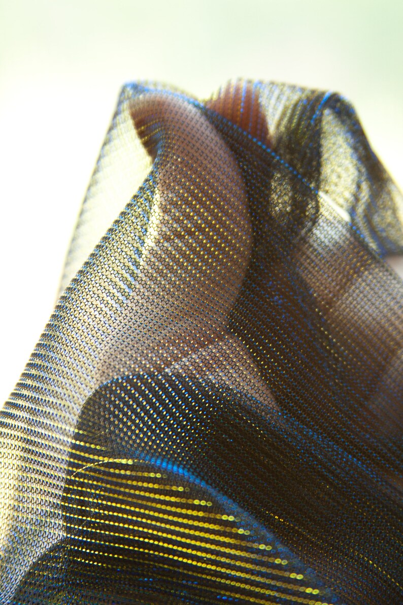 May include: A close-up of a black and gold fabric with a shimmery, iridescent finish. The fabric has a fine mesh texture and is draped over a surface.