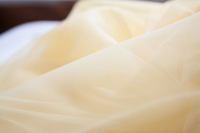 May include: Close-up of a soft, pale yellow tulle fabric with a delicate, woven texture.