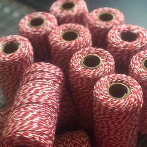 May include: A close-up of a pile of red and white baker's twine spools. The twine is a classic red and white striped pattern.