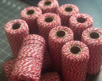 May include: A close-up of a pile of red and white baker's twine spools. The twine is a classic red and white striped pattern.