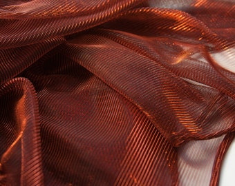 May include: Close-up of a metallic, copper-colored fabric with a woven, striped pattern. The fabric is draped and folded, creating a textured, shimmering effect.