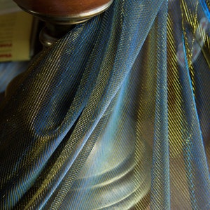 May include: A close-up of a gold and blue metallic fabric draped over a brown object. The fabric has a shimmery, iridescent quality.