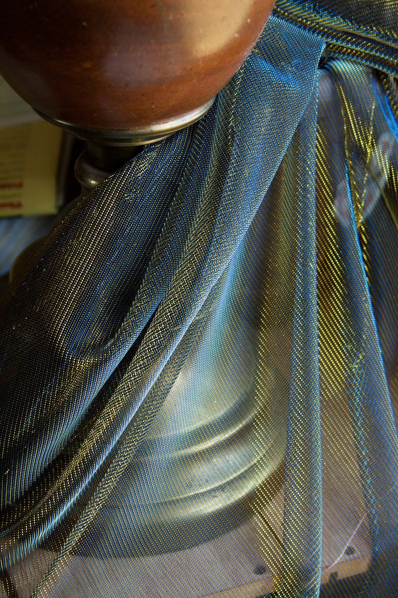 May include: A close-up of a gold and blue metallic fabric draped over a brown object. The fabric has a shimmery, iridescent quality.