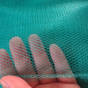 May include: Close-up of a green netting material with a hexagonal pattern. The netting is soft and flexible, and it is being held in a hand.