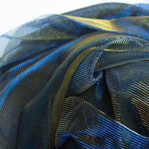 May include: A close-up of a blue and gold metallic fabric with a shiny, iridescent finish. The fabric is folded and draped, creating a textured and abstract pattern.