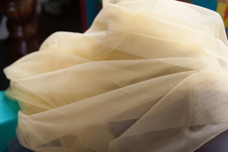 May include: A close-up of a pale yellow tulle fabric. The fabric is soft and delicate, with a fine mesh texture.