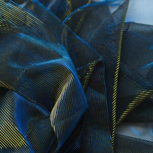 May include: Close-up of a blue and gold metallic mesh fabric. The fabric is folded and draped, showing the texture and sheen of the material.