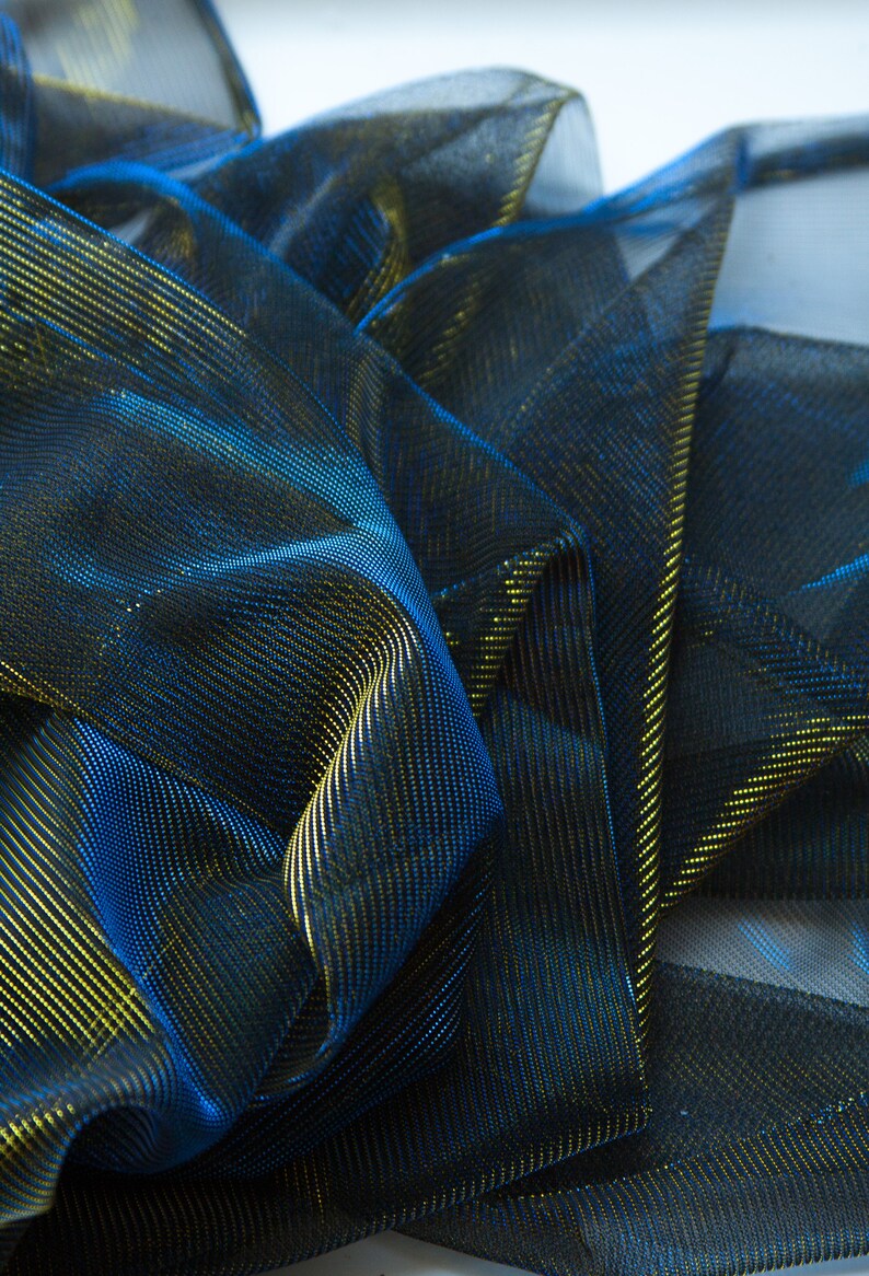 May include: Close-up of a blue and gold metallic mesh fabric. The fabric is folded and draped, showing the texture and sheen of the material.
