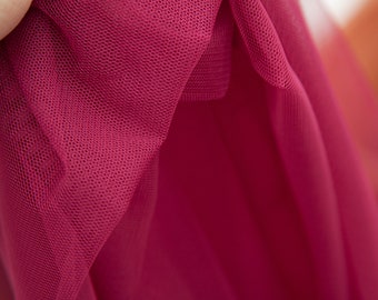 May include: Close-up of a deep pink tulle fabric with a fine mesh texture. The fabric is draped and folded, creating soft folds and curves.