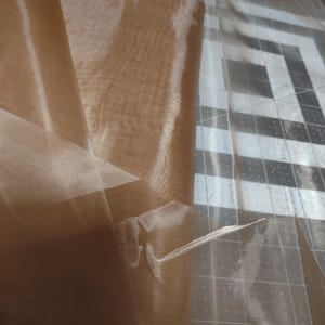 May include: A sheer brown fabric with a slightly textured surface. The fabric is folded and draped over a gridded surface.