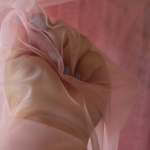 May include: A close-up of a soft, pink tulle fabric. The fabric is gathered and draped, creating a delicate and airy look.