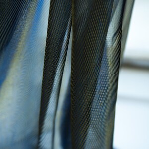 May include: Close-up of a sheer black curtain with a subtle gold pattern. The fabric is translucent, allowing light to filter through.