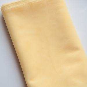 May include: A pale yellow tulle fabric, folded and displayed on a white surface.