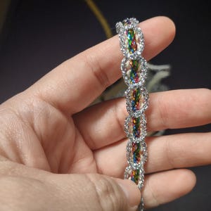 May include: A silver and multi-colored braided trim with a repeating oval pattern.