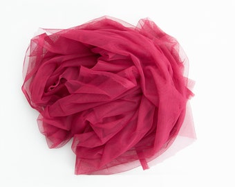 May include: A pile of soft, crimson tulle fabric. The fabric is loosely gathered and has a delicate, airy texture.