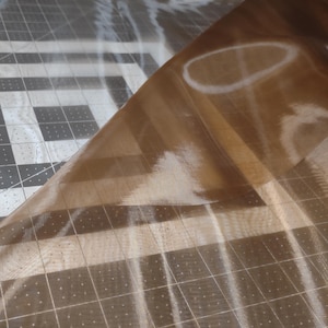 May include: A piece of brown sheer fabric with a grid pattern. The fabric is folded over itself and appears to be translucent.
