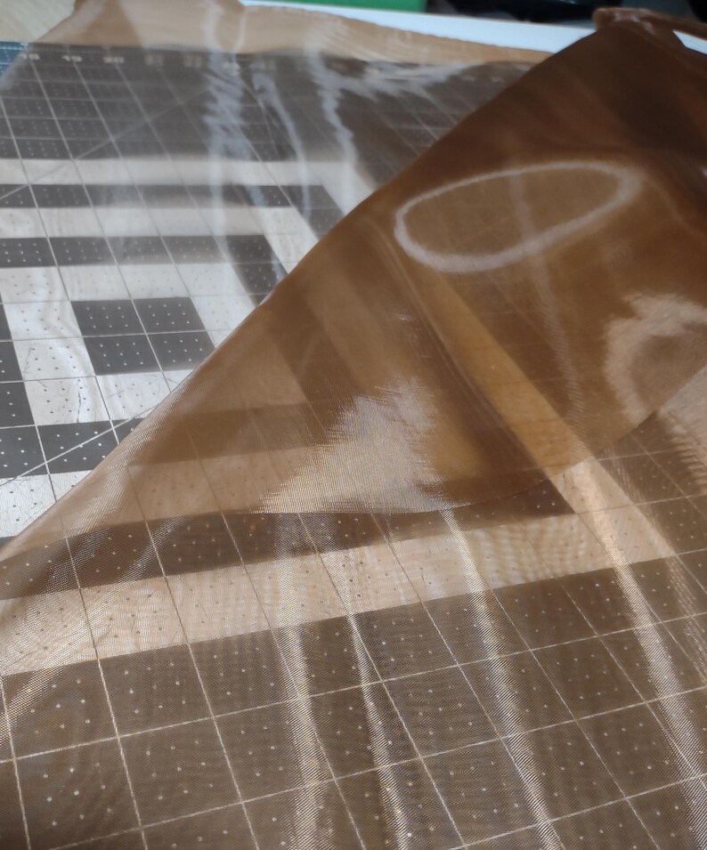 May include: A piece of brown sheer fabric with a grid pattern. The fabric is folded over itself and appears to be translucent.