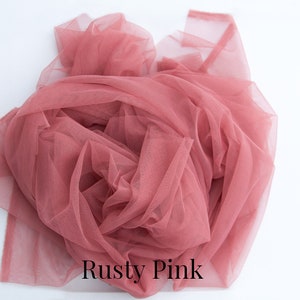 May include: A close-up of a dusty pink tulle fabric. The fabric is soft and delicate, and it is perfect for crafting or decorating.