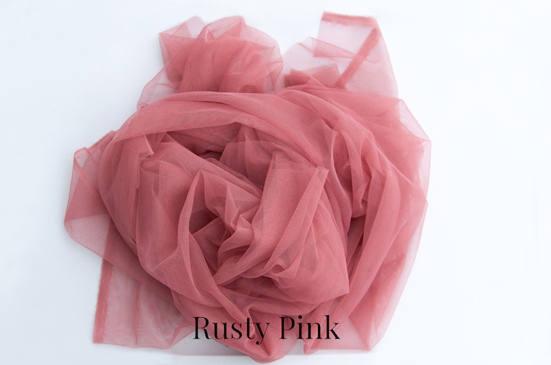 May include: A close-up of a dusty pink tulle fabric. The fabric is soft and delicate, and it is perfect for crafting or decorating.
