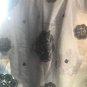 May include: Black sheer fabric with a repeating pattern of black velvet flowers. The fabric is translucent and has a delicate texture.