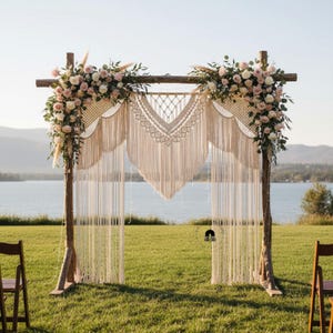 Könnte beinhalten: Eine rustikale Hochzeitsbogen aus Holz, verziert mit cremefarbenem Makramee und Blumenschmuck aus rosa und weißen Rosen. Der Bogen steht auf einer Wiese, mit einem See und Bergen im Hintergrund, was eine romantische Kulisse schafft.