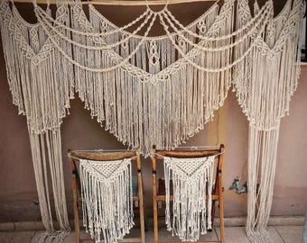 May include: A macrame wedding backdrop with two chairs decorated with macrame. The backdrop is made of natural cotton rope and has a bohemian style.