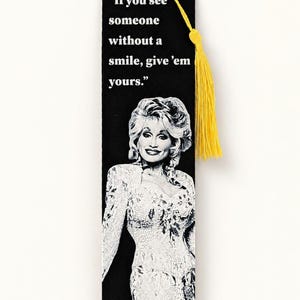 May include: A rectangular black bookmark featuring a white graphic illustration of Dolly Parton and the printed text, "If you see someone without a smile, give 'em yours." A bright yellow tassel is attached to the top through a small hole.