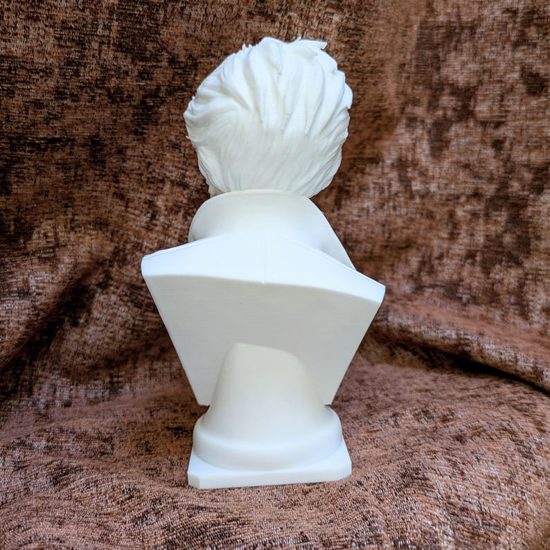 May include: A white matte bust sculpture showing the back view of a person with short, textured hair and a collared garment. The figure is positioned on a pedestal base, featuring a smooth, solid surface and clean, defined lines throughout.