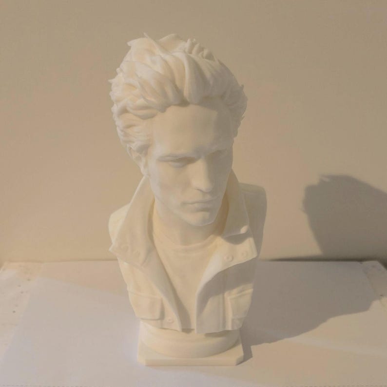 May include: A matte white bust sculpture of a person with textured, swept-back hair. The figure wears a collared jacket with visible buttons and pockets, captured in a head-and-shoulders portrait style with a neutral, solid white finish.