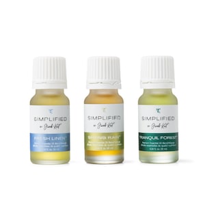 Puede incluir: Tres pequeños frascos de vidrio de aceite esencial con tapas blancas. Los frascos están etiquetados "SIMPLIFIED by Jacob Kait" y tienen los aromas "FRESH LINEN", "SPRING RAIN" y "TRANQUIL FOREST".