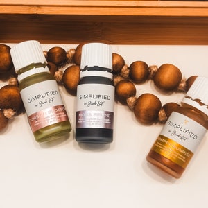 May include: Three essential oil bottles with white labels and lids. The bottles are labeled "Tunisian Blossom", "Mona Fields", and "Pompeii Sunrise" by "Simplified by Jacob Kat". The bottles are 1 fl. oz. (30 ml).