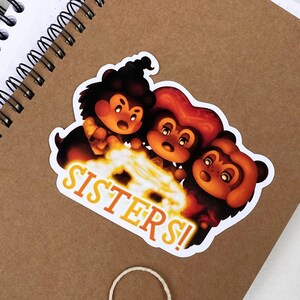 以下が含まれることがあります： 3匹の漫画の動物、キツネ、クマ、アライグマが描かれた白いステッカーで、「SISTERS!」という黄色の文字が書かれています。動物はオレンジ、茶色、黒の毛皮で漫画のスタイルで描かれています。