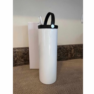 May include: White stainless steel tumbler with a black lid and a black handle. The tumbler has a straw sticking out of the lid.
