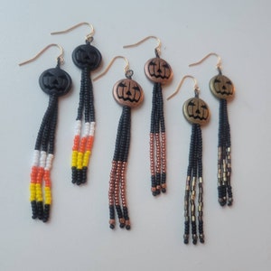 Op de afbeelding: Een verzameling Halloween-oorbellen. De oorbellen hebben pompoenvormige bedels in zwart- en bronstinten, met kralenfranjes in zwart, oranje, wit, geel en brons. De oorbellen hebben goudkleurige oorhaken.