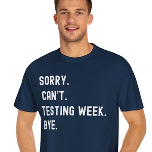 May include: A navy blue short-sleeved t-shirt featuring white text printed on the front that reads: SORRY. CAN'T. TESTING WEEK. BYE. The garment has a classic crew neckline and a standard fit, providing a clean and simple look for casual wear.