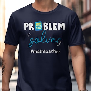 May include: Navy blue t-shirt with the words "PROBLEM solver" and a calculator graphic. The text "#mathteacher" is below the word "solver". The shirt is a crew neck.