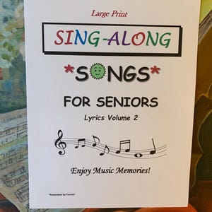 May include: A white booklet with the title "SING-ALONG *SONGS* FOR SENIORS" in colorful letters. The subtitle is "Lyrics Volume 2" and the text "Enjoy Music Memories!" is at the bottom.