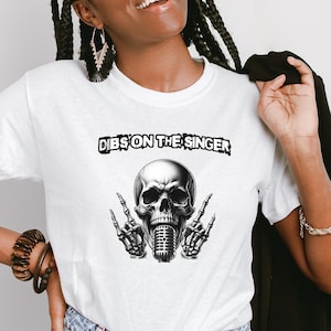 May include: White t-shirt featuring a black and white skull graphic holding a microphone. The text "Dibs on the singer" is printed above the skull.