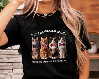 May include: Black t-shirt featuring four illustrated cats wearing bow ties. The cats are gray, orange, black and white, and gray and white. Text above reads "WHY HAVE ONE COLOR OF CAT..." and below reads "...WHEN YOU CAN HAVE THE WHOLE SET?"