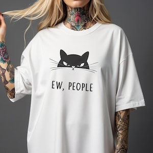 Peut inclure: T-shirt blanc avec un motif de chat noir et le texte "EW, PEOPLE". Le chat a une expression renfrognée. Le t-shirt est de style décontracté et surdimensionné.