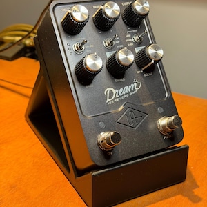May include: Black Dream '65 Reverb-Amp guitar effects pedal with multiple knobs, switches, and foot switches. The pedal is mounted on a black stand. The text "Dream" and "65 REVERB-AMP" are visible on the pedal.